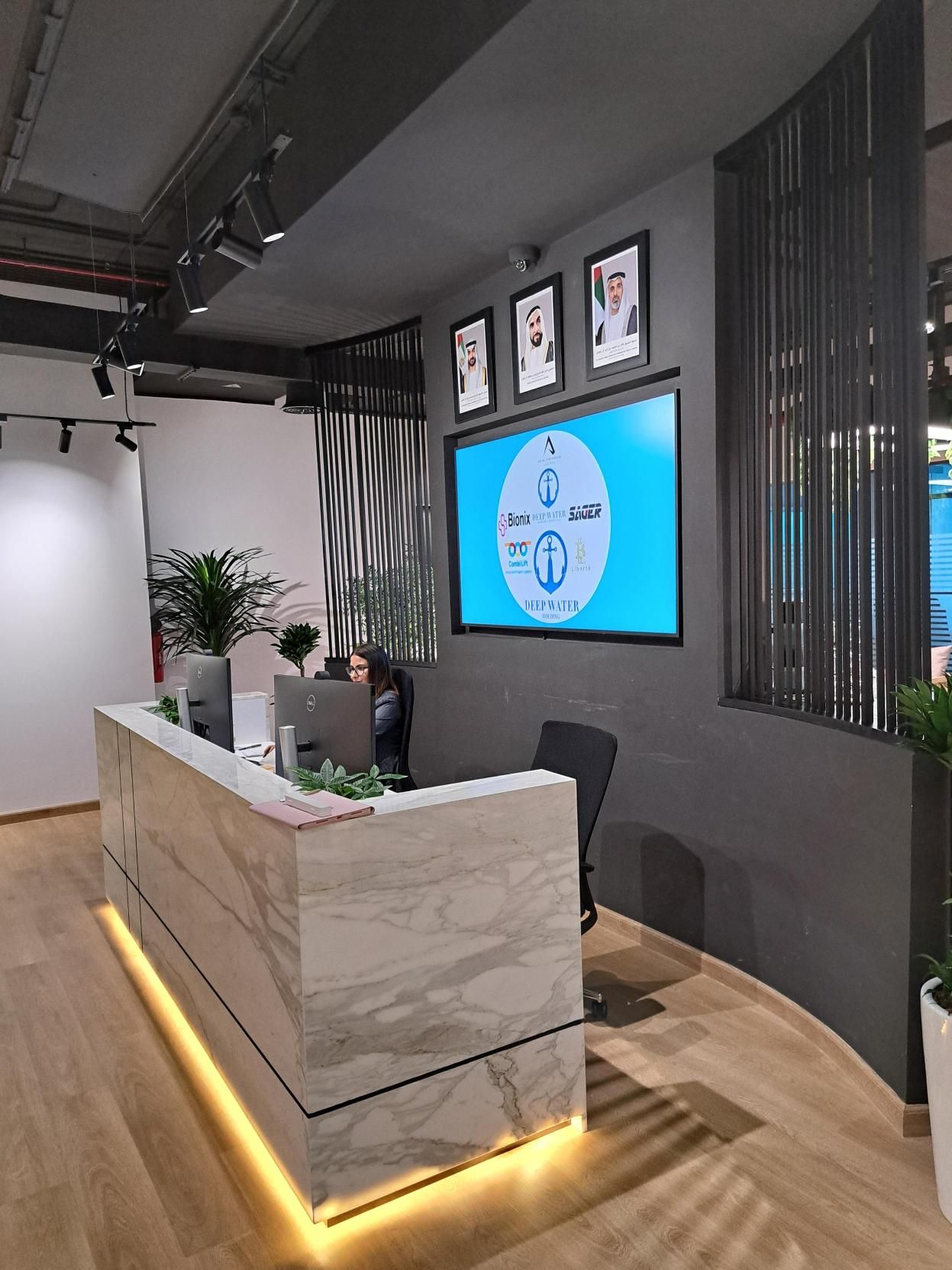 Modern marble reception desk with backlit base, large display screen, and framed photos on the wall.