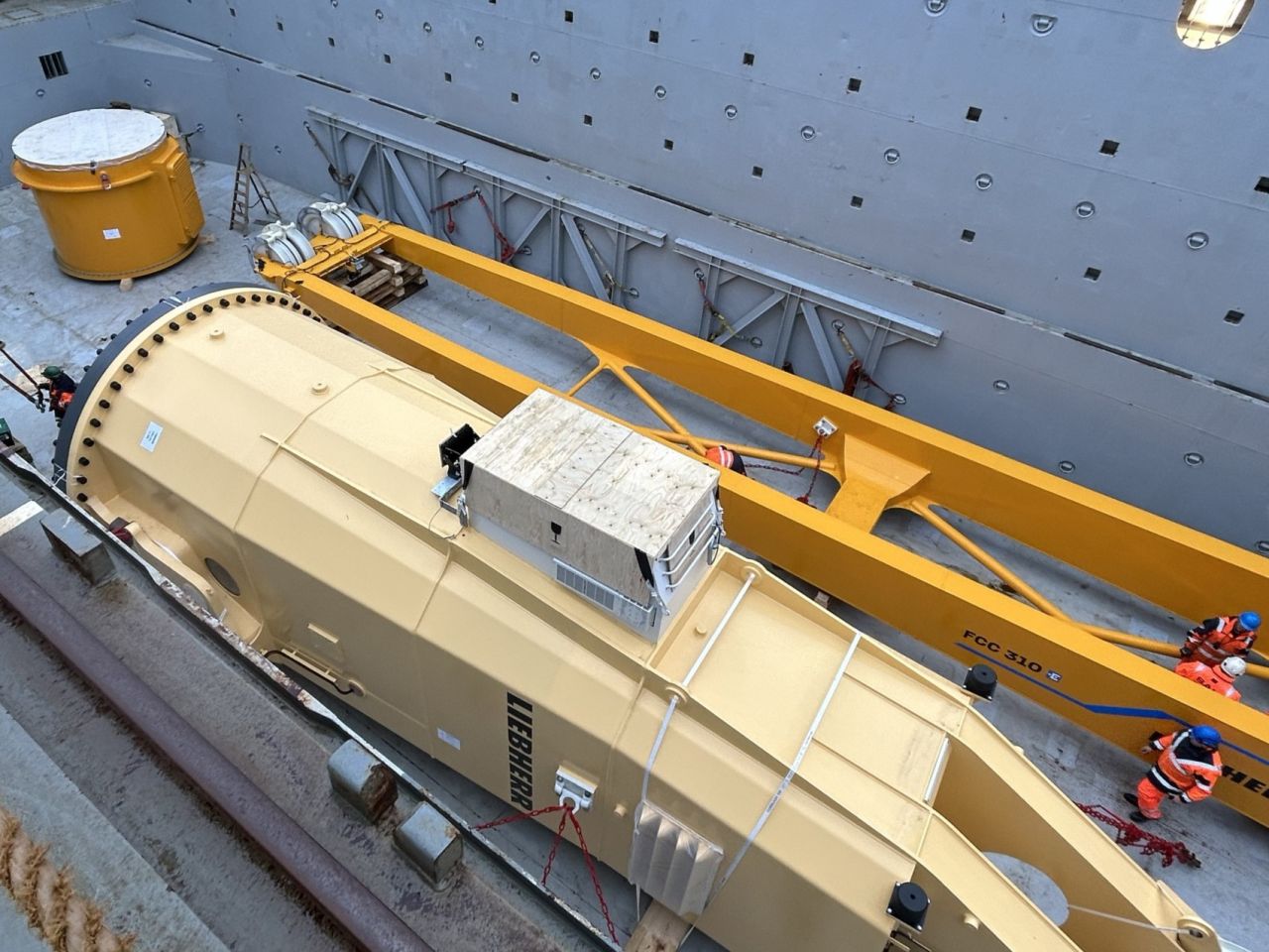 Large yellow Liebherr slewing column and components secured inside a cargo vessel’s hold with lashings and support structures.